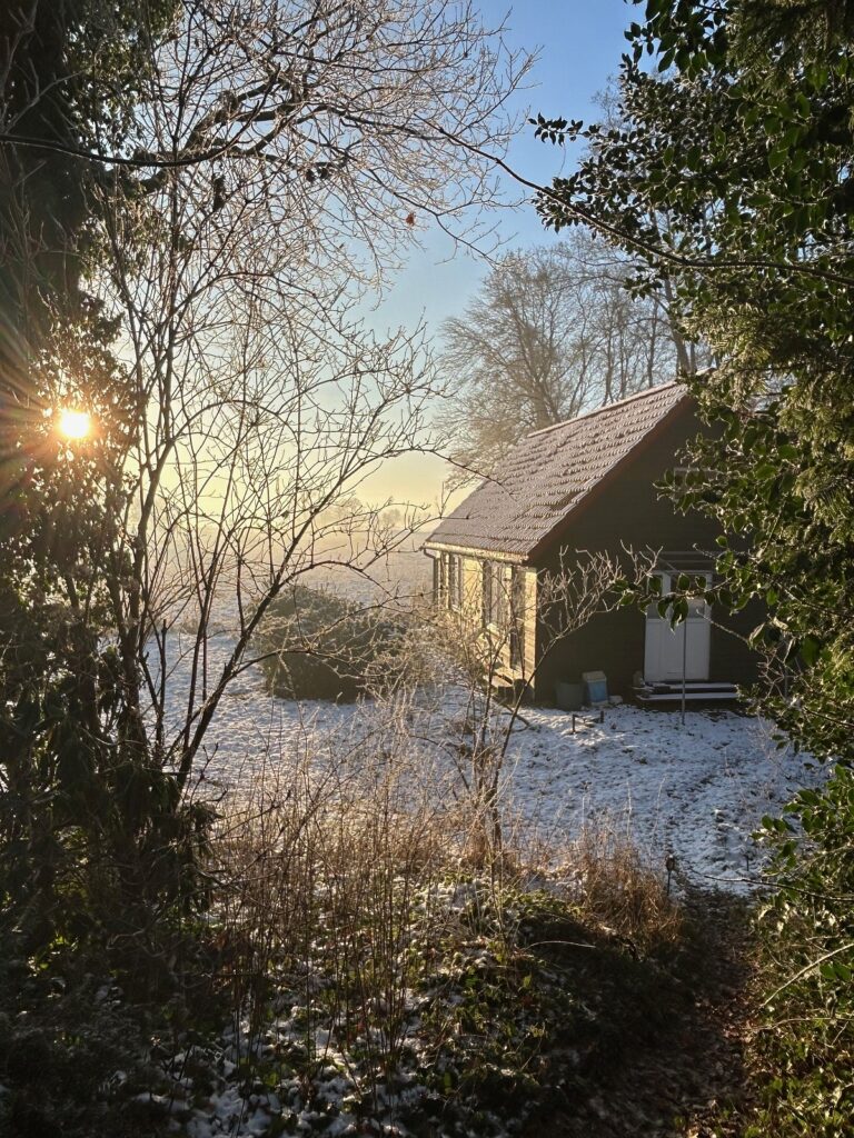 Winterliche Gartenlandschaft auf dem Ferienhof Ohlenbusch mit leicht verschneitem Ferienhaus, kahlen Bäumen und tief stehender Sonne