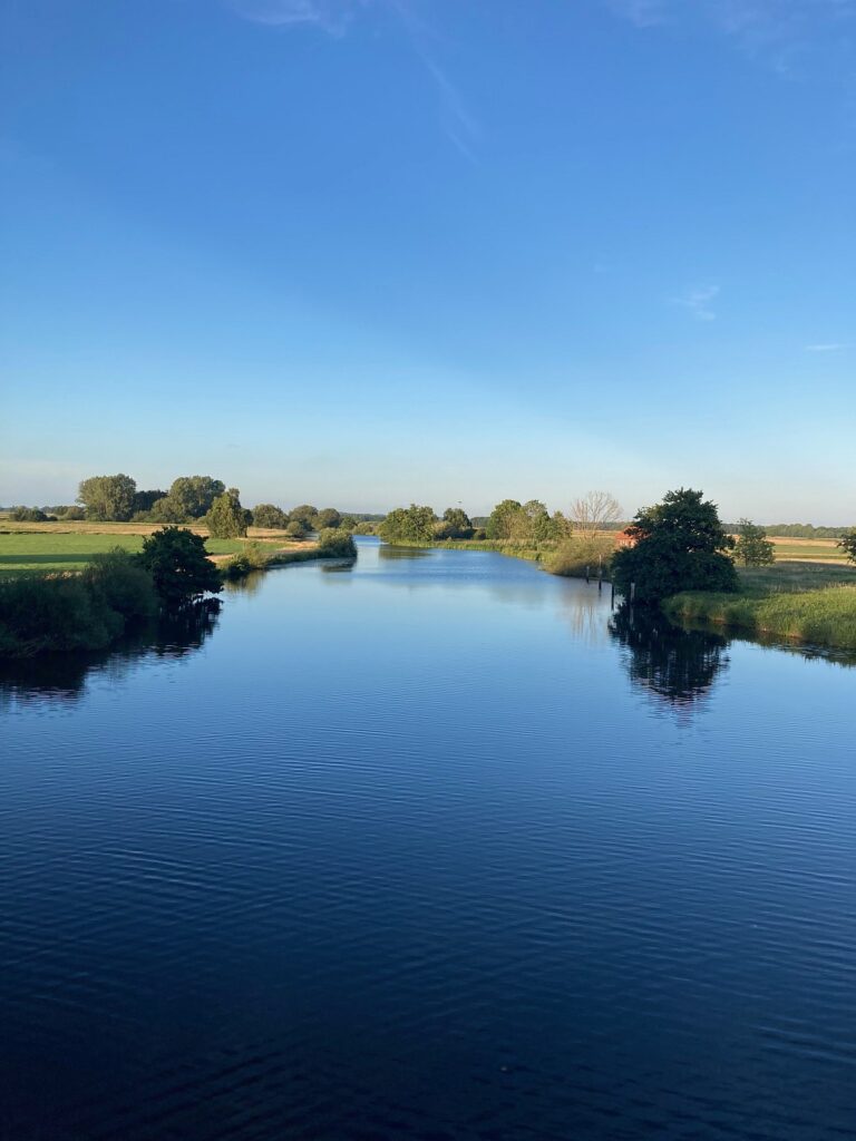 Ruhiger Fluss in der Landschaft rund um Worpswede, gesäumt von grünen Wiesen und Bäumen unter blauem Himmel